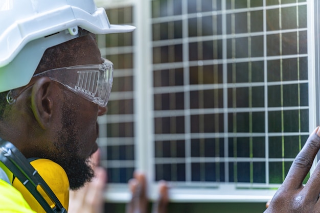 Trabajador de fábrica comprobando el panel de células solares para tecnología sostenible con traje de trabajo y casco