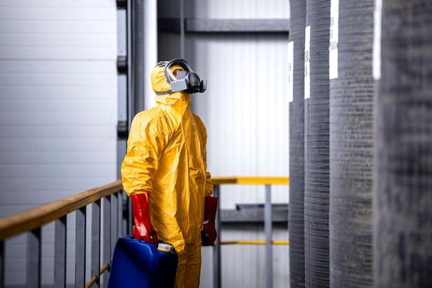 Trabajador de fábrica en equipo de protección comprobando la cantidad de productos químicos dentro de un gran depósito