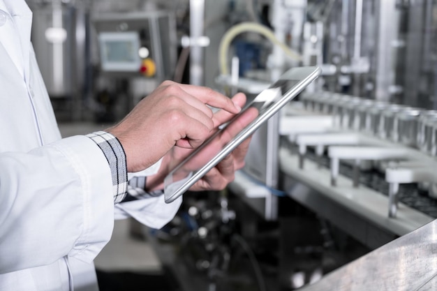 Trabajador de fábrica inspeccionando línea de producción en fábrica de bebidas con tableta de computadora