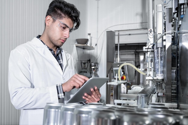 Trabajador de fábrica inspeccionando línea de producción en fábrica de bebidas con tableta de computadora