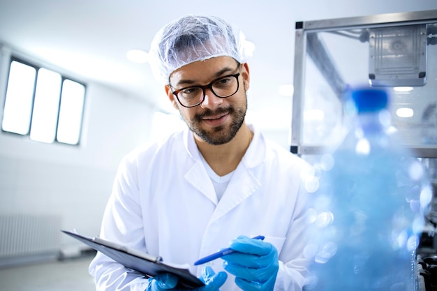 Trabajador de fábrica con lista de verificación haciendo control de calidad del agua potable en la planta embotelladora