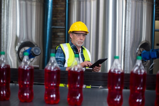 Trabajador de fábrica masculino que controla las botellas de bebida fría