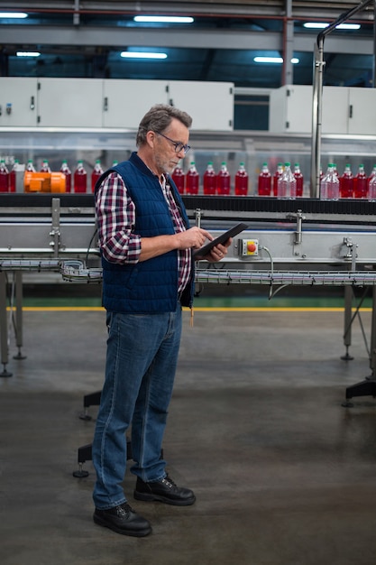 Trabajador de fábrica usando tableta digital al lado de la línea de producción