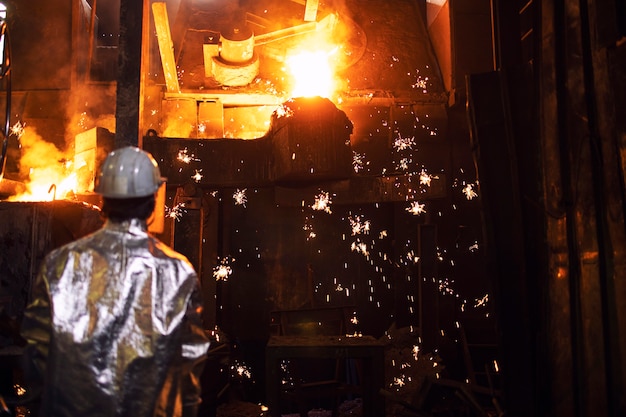 Trabajador de fundición controlando la fusión del hierro en el horno y las chispas que vuelan alrededor.