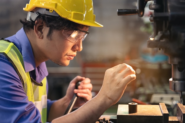 Un trabajador con gafas de pie cerca de equipos industriales y verifica la producción. Hombre operando la máquina en la fábrica.