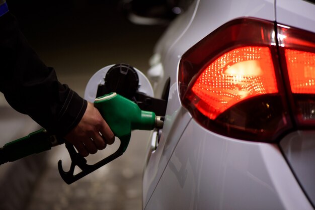 Trabajador de gasolinera en ropa de trabajo repostaje de coches de lujo con gasolina sosteniendo la pistola de llenado en la estación.