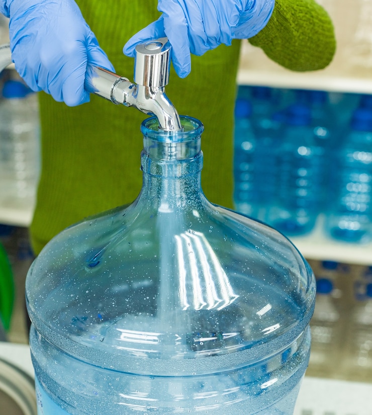 Foto trabajador con guantes de goma extrae agua limpia en una botella grande después de la filtración