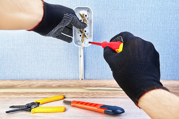 Trabajador con guantes protectores está girando el tornillo en una nueva toma de corriente con un destornillador.