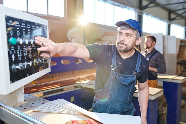 Trabajador guapo serio que configura la máquina de fábrica