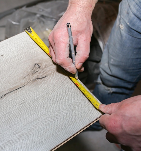 Trabajador haciendo pisos laminados en el apartamento Cinta métrica y lápiz en las manos Renovación de reparación de mantenimiento Tablones de parquet de madera en el interior