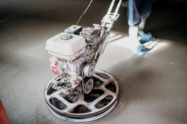 Trabajador con herramienta de paleta eléctrica acabado de piso de concreto superficie de concreto liso en la construcción de viviendas