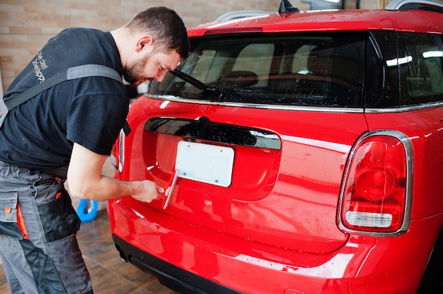 Trabajador de hombre lavando coche rojo en el garaje de detalle