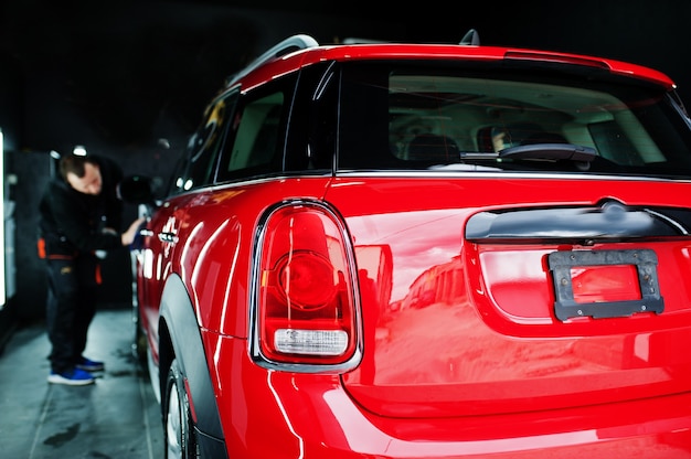 Trabajador de hombre lavando coche rojo en el garaje de detalle