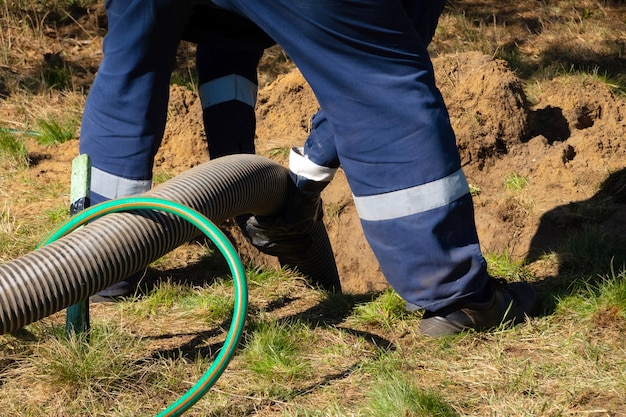 Trabajador de hombre sosteniendo el tubo, proporcionando servicio de limpieza de alcantarillado al aire libre. La máquina de bombeo de aguas residuales está destapando la boca de acceso bloqueada