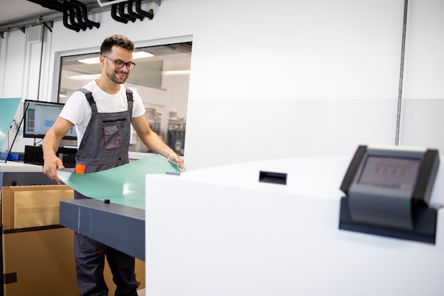 Trabajador de impresión sonriente que opera la computadora a la máquina de placa en la imprenta.