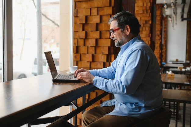 Trabajador independiente masculino senior que trabaja en una computadora portátil en el concepto de trabajo remoto de café