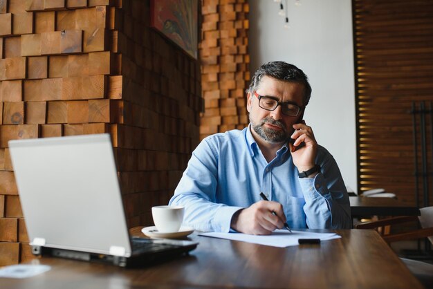 Trabajador independiente masculino senior que trabaja en una computadora portátil en el concepto de trabajo remoto de café