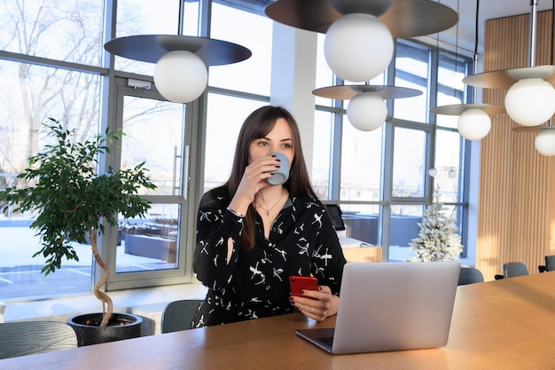 Un trabajador independiente trabaja en un café, una morena bebe café sentada frente a una computadora portátil