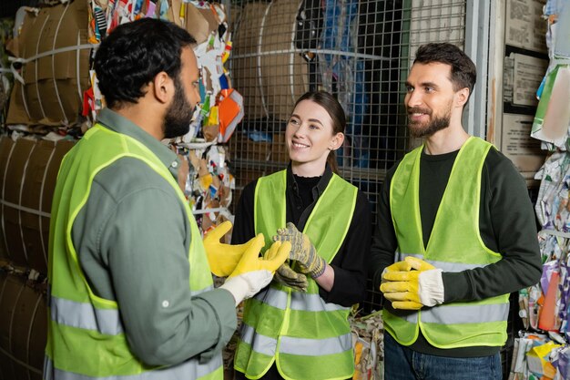 Trabajador indio con chaleco y guantes de alta visibilidad hablando con colegas sonrientes mientras está de pie