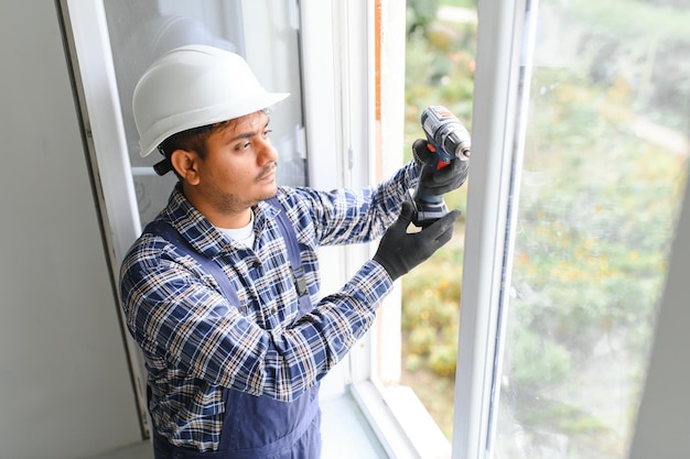 Trabajador indio con monos instalando o ajustando ventanas de plástico en el salón de casa