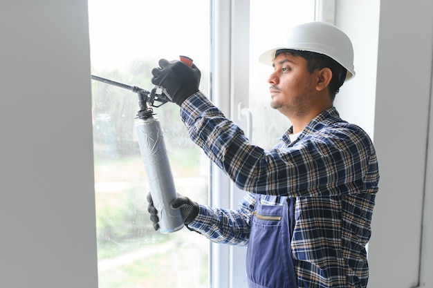 Trabajador indio que utiliza un tubo de silicona para reparar ventanas interiores