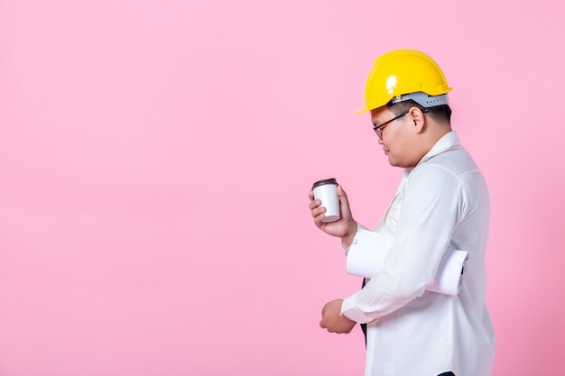 Trabajador de la industria o ingeniero que trabaja un arquitecto constructor que estudia el plan de diseño ingeniero civil serio sosteniendo una taza de café trabajando con la lectura en el plano aislado en el estudio de espacio de copia en blanco rosa