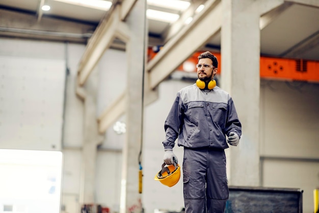 Un trabajador de la industria pesada con casco en las manos yendo a su lugar de trabajo en la fábrica.