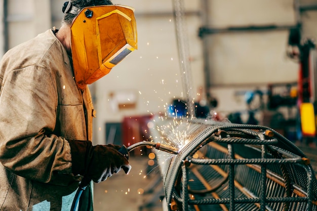 Un trabajador de la industria pesada está soldando una estructura de metal mientras está parado en las instalaciones