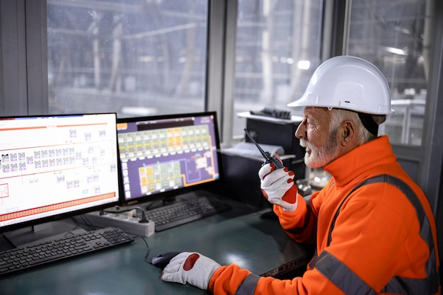 Trabajador industrial en equipo de seguridad sentado en la sala de control de fábrica monitoreando el proceso de producción