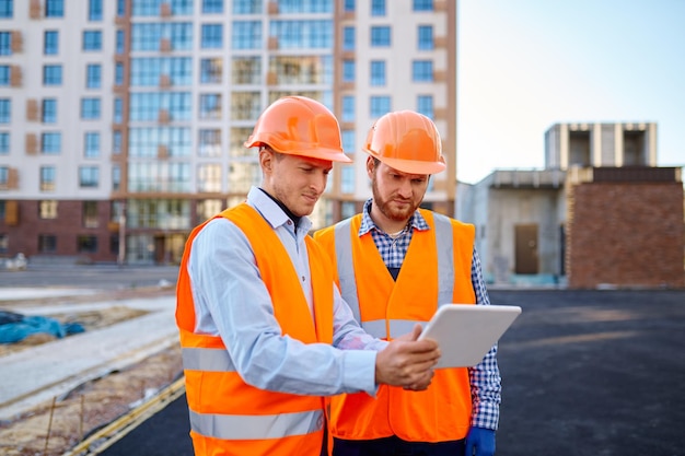 Trabajador informando al contratista sobre la ejecución del plan de construcción usando una tableta en el sitio de construcción