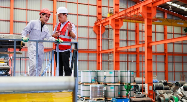 Trabajador de ingeniería de fábrica que opera una máquina de techo de chapa metálica en la fábrica de fabricación de la industria pesada Trabajador en casco de seguridad en las instalaciones industriales de la fábrica