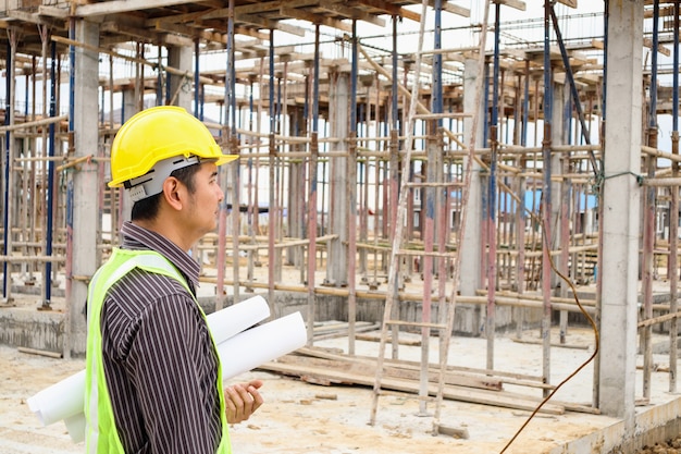 Trabajador de ingeniero de construcción de hombre de negocios asiático en casco protector y papel de planos en mano en el sitio de construcción de viviendas