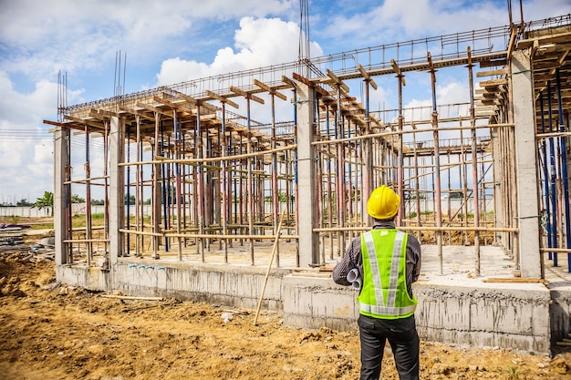 Trabajador de ingeniero de construcción de hombre de negocios asiático en casco protector y papel de planos en mano en el sitio de construcción de viviendas