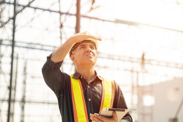 Foto trabajador del ingeniero del constructor del capataz que mira el trabajo duro del día soleado del día soleado del sitio de construcción del edificio grande.