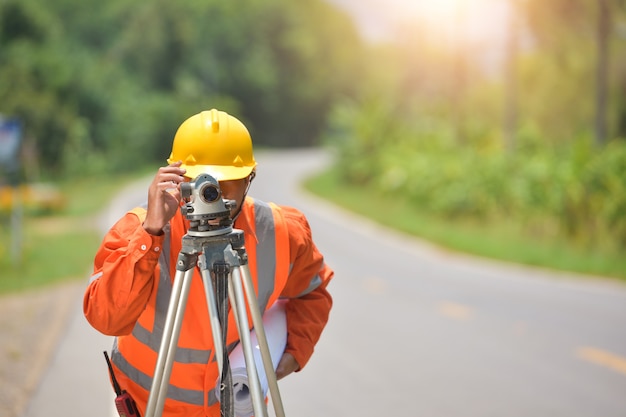 Foto trabajador de ingeniero topógrafo haciendo medición con teodolito en obras viales. ingeniero de encuesta en sitio de construcción.