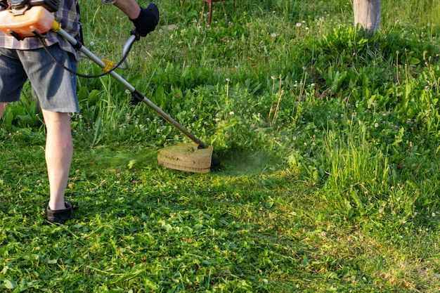 El trabajador de un jardín corta una hierba. El hombre con el uniforme del trabajador general trabaja en el césped. Trabajos de los servicios municipales de mejora de territorios.