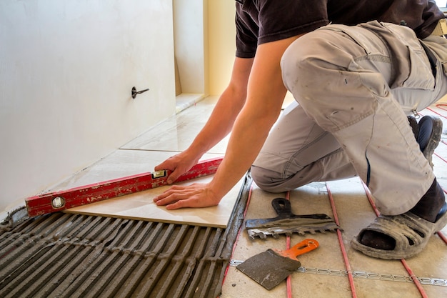 Trabajador joven instalador de baldosas cerámicas con palanca en el piso de cemento con calefacción sistema de cable rojo