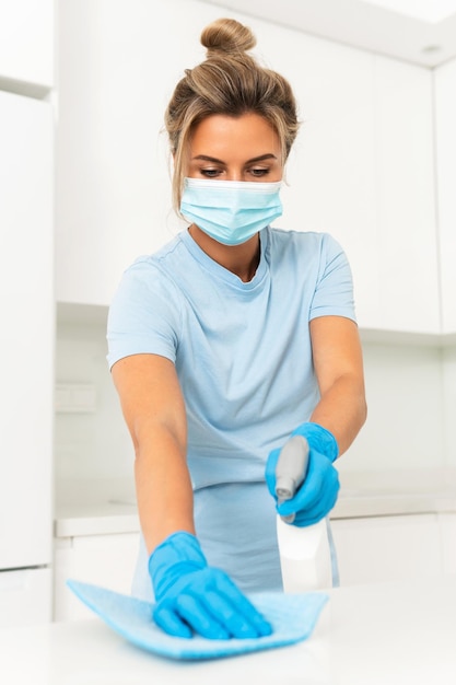 Trabajador joven vistiendo guantes y máscara de prevención durante la limpieza del apartamento