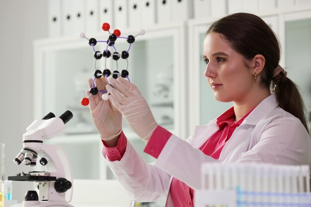 Trabajador de laboratorio en bata blanca examina modelo de molécula positiva mujer trabaja con químico