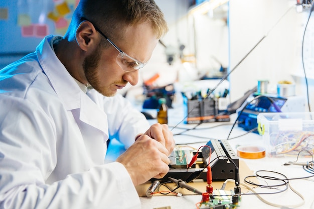 Foto el trabajador de laboratorio electrónico conecta la placa de circuito con cables y abrazaderas para realizar pruebas y mediciones