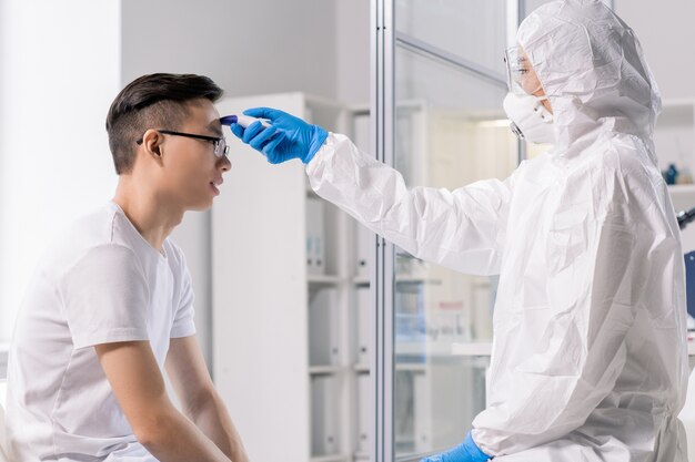 Trabajador de laboratorio con overoles de protección, mascarilla, guantes y anteojos con herramientas médicas especiales durante el examen