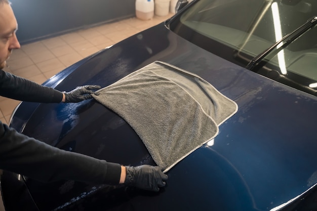 Trabajador de lavado de coches limpia el coche después de lavarlo con una toalla de microfibra.