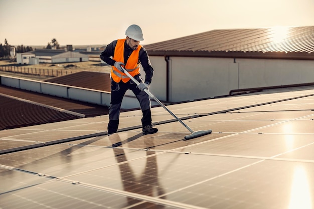 Un trabajador limpiando paneles solares en el techo al atardecer