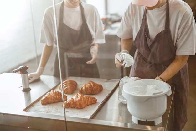 Trabajador llena pastelería con deliciosa crema en la mesa con croissants en panadería artesanal