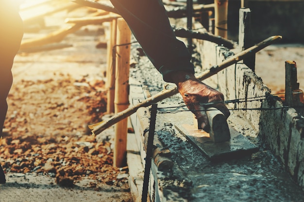 Trabajador de la mano que nivela el concreto para la mezcla de cemento en el sitio de construcción