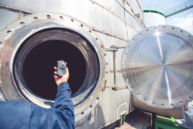 Trabajador mano sujetando el detector de gas de seguridad de inspección de pruebas de gas en la boca del tanque de acero inoxidable para trabajar dentro