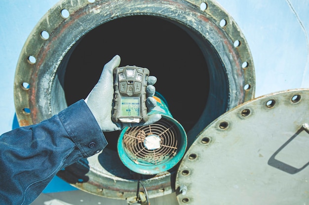 Trabajador mano sujetando el detector de gas de seguridad de inspección de pruebas de gas en la boca del tanque de acero inoxidable para trabajar dentro