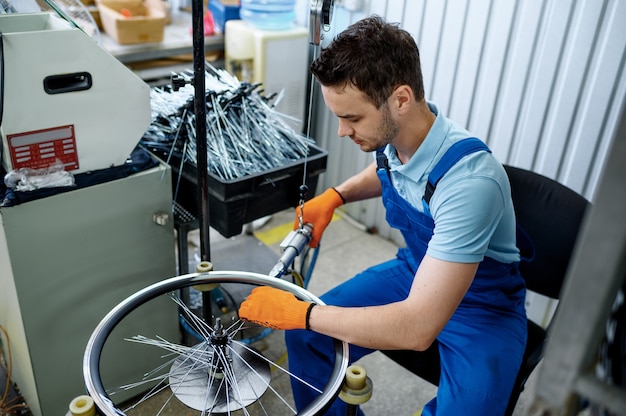 Trabajador con máquina herramienta instala nuevos radios de bicicleta en fábrica. Montaje de ruedas de bicicleta en taller, instalación de piezas de ciclo