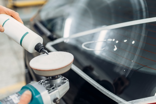 Trabajador con máquina pulidora restaura la ventana trasera del coche. Detalles automáticos sobre el servicio de lavado de autos