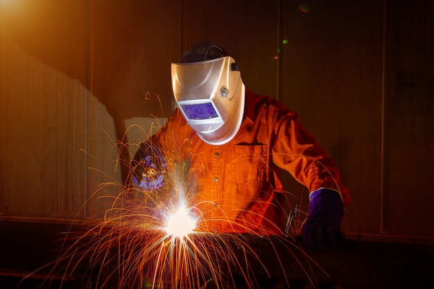 Trabajador con máscara protectora de soldadura de metal en almacén industrial.